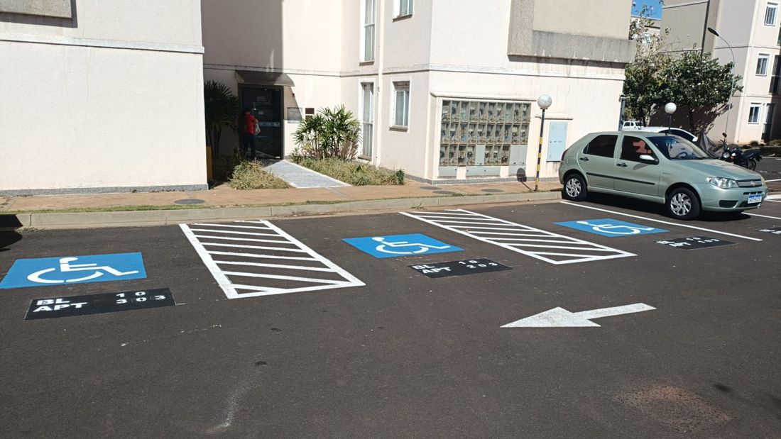Vagas para pessoas com deficiência pintadas em condomínio, com área de transferência e número do apartamento