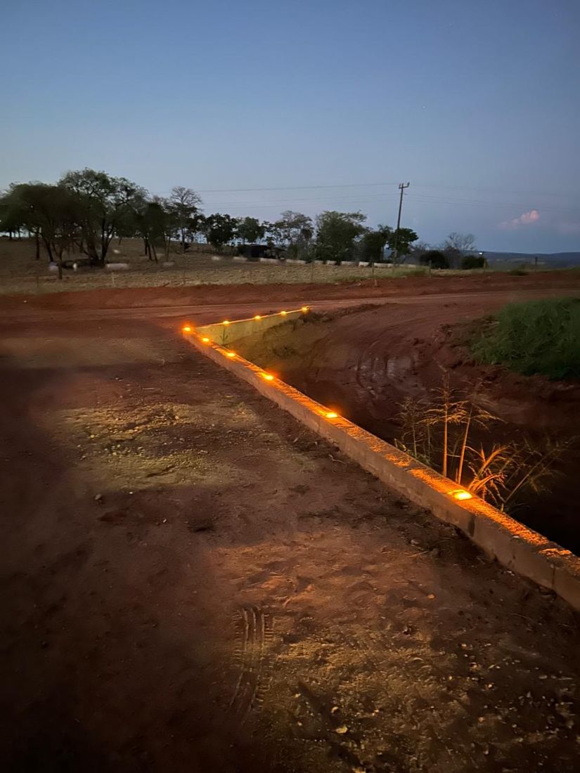 Guia ao lado de vala com tachas de Led's acesas em estrada de terra